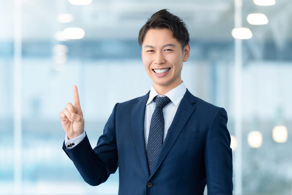人差し指を立てる爽やかなスーツ姿の男性